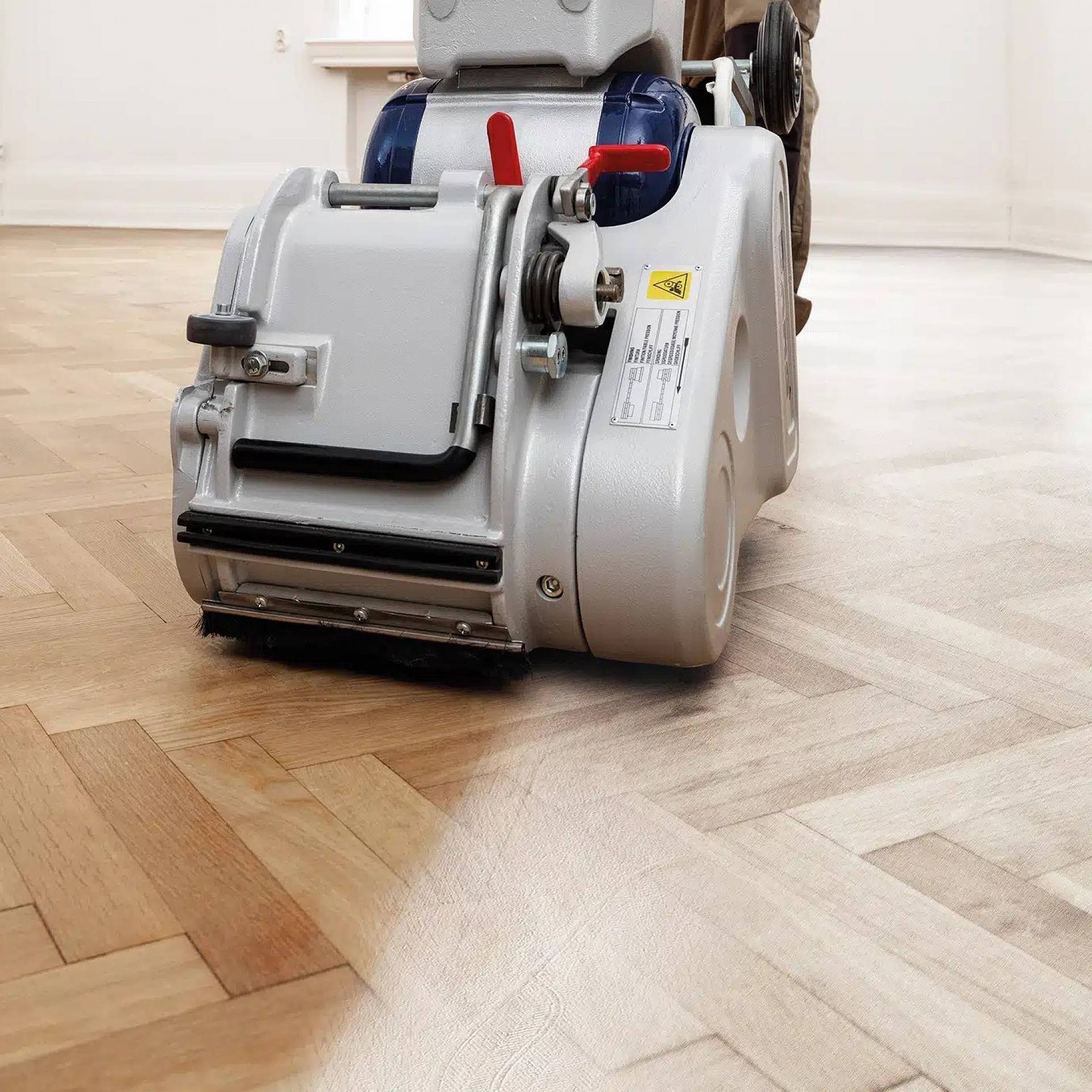 Handwerker schleift Parkettboden mit Schleifmaschine in hellem Raum