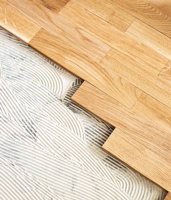 Holzparkett wird in frischen Kleber auf dem Boden verlegt, Zahnspachtel-Struktur ist deutlich sichtbar.