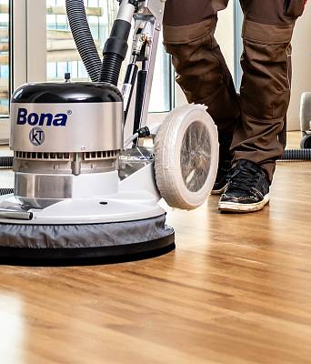 Handwerker schleift einen Holzboden mit Bodenschleifmaschine, Staubsaugerschlauch angeschlossen für saubere Parkettarbeit.