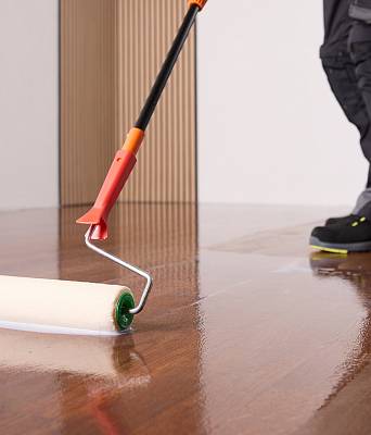 Farbroller trägt glänzenden Lack auf dunklen Parkettboden auf und hinterlässt spiegelnde Oberfläche