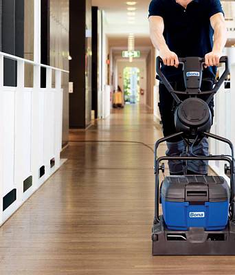 Handwerker reinigt Parkettboden mit professioneller Maschine in modernem Arbeitsgebäude und sorgt für eine gepflegte Oberfläche.