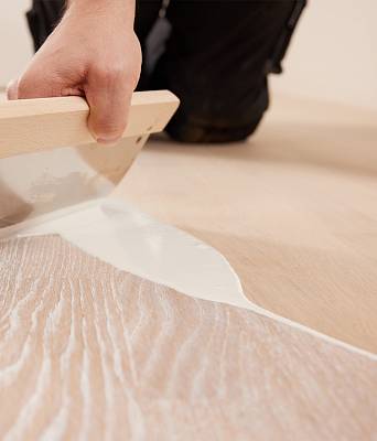 Handwerker trägt mit Spachtel pigmentiertes Öl auf helle Holzdielen auf und verleiht dem Parkett neuen Glanz.