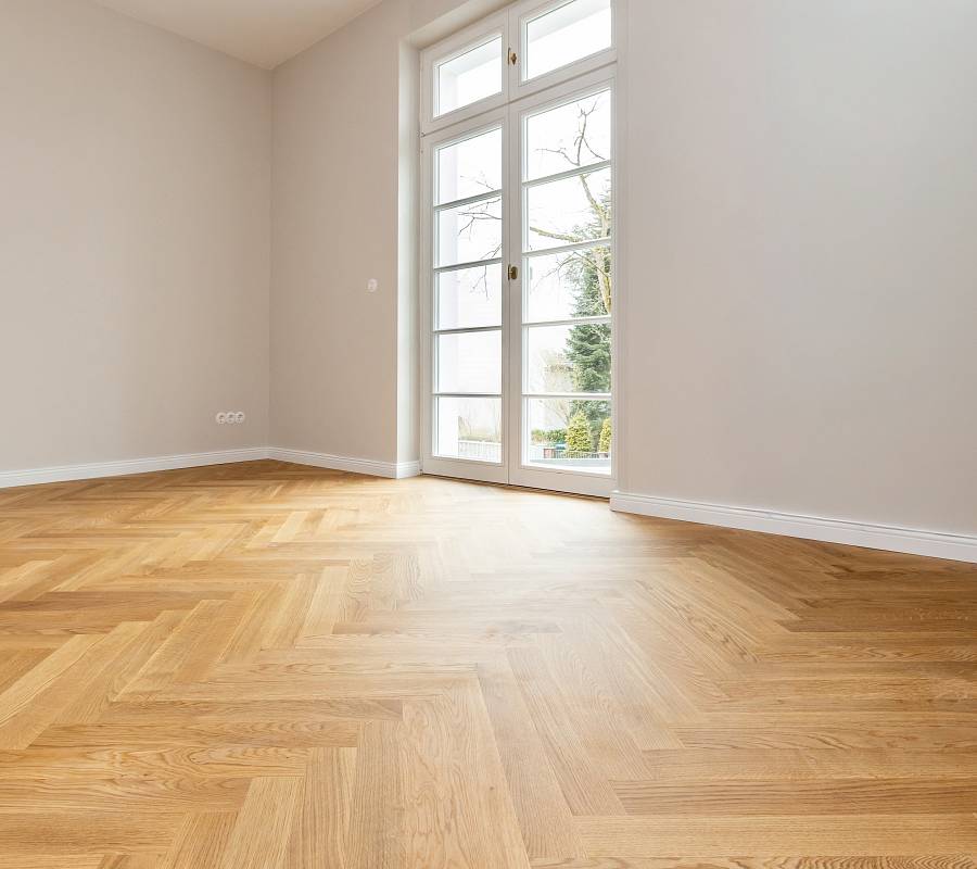 Leerer, heller Raum mit großem Fenster und Stäbchenparkett aus Eiche, das den Raum warm und offen wirken lässt.