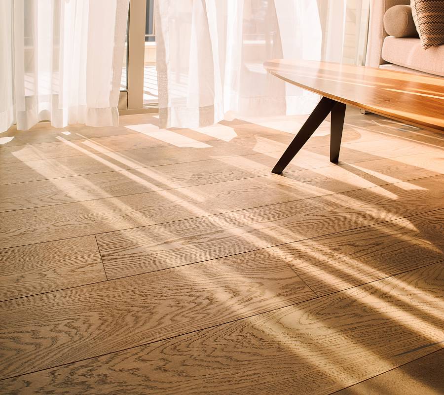 Wohnraum mit natürlicher Landhausdiele aus Eiche, warmem Sonnenlicht, modernem Couchtisch und ruhiger Wohnatmosphäre.