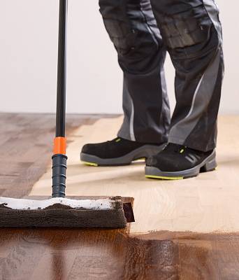 Handwerker färbt mit einer Schwammrolle einen hellen Parkettboden dunkel