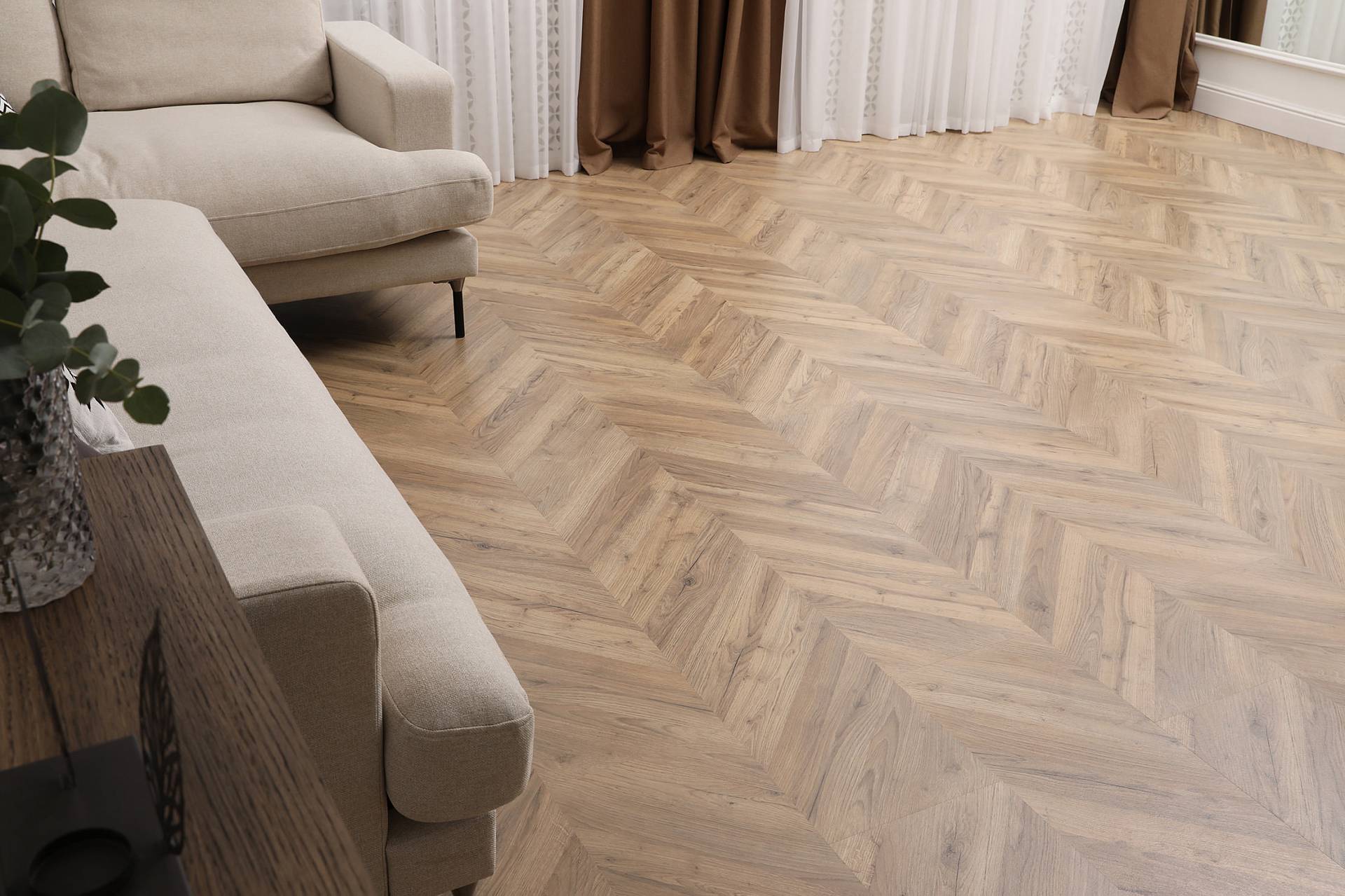 Wohnraum mit hellem Fischgrätparkett und modernem Sofa im warmen Naturton.