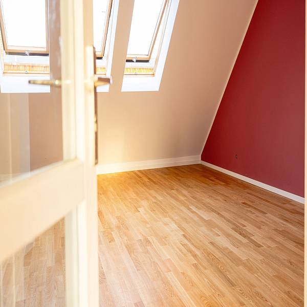 Moderner Wohnraum mit natürlichem Eichenparkett, großen Fensterflächen, Zimmerpflanze und klarer, ruhiger Raumgestaltung.