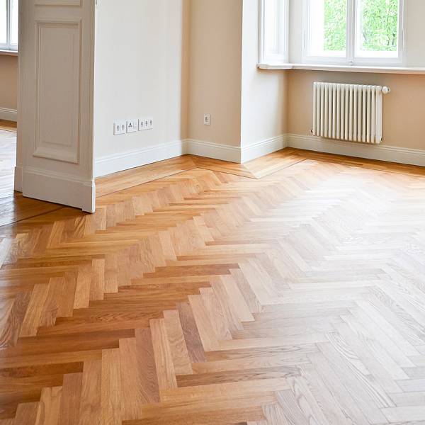 Großzügiger Wohnraum mit klassischem Fischgrätparkett aus Eiche, bodentiefen Fenstern, Sofa und heller, moderner Einrichtung.