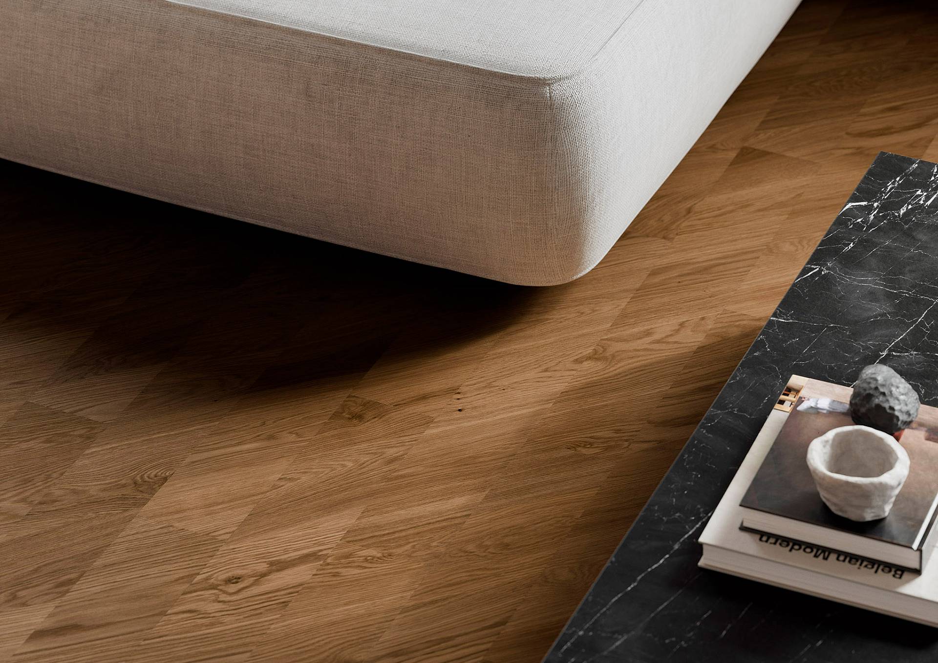 Detailansicht eines dunklen Eichen-Fischgrätparketts neben hellem Sofa und schwarzem Marmortisch in modernem Wohnambiente.