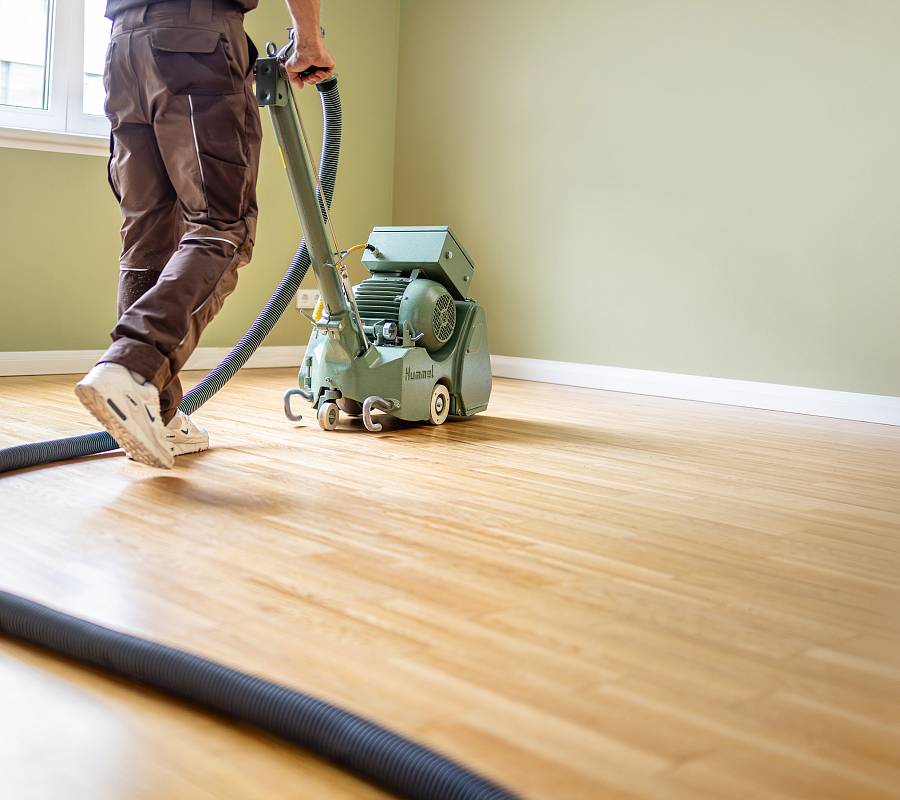 Handwerker schleift hellen Parkettboden mit Bodenschleifmaschine in leerem Raum