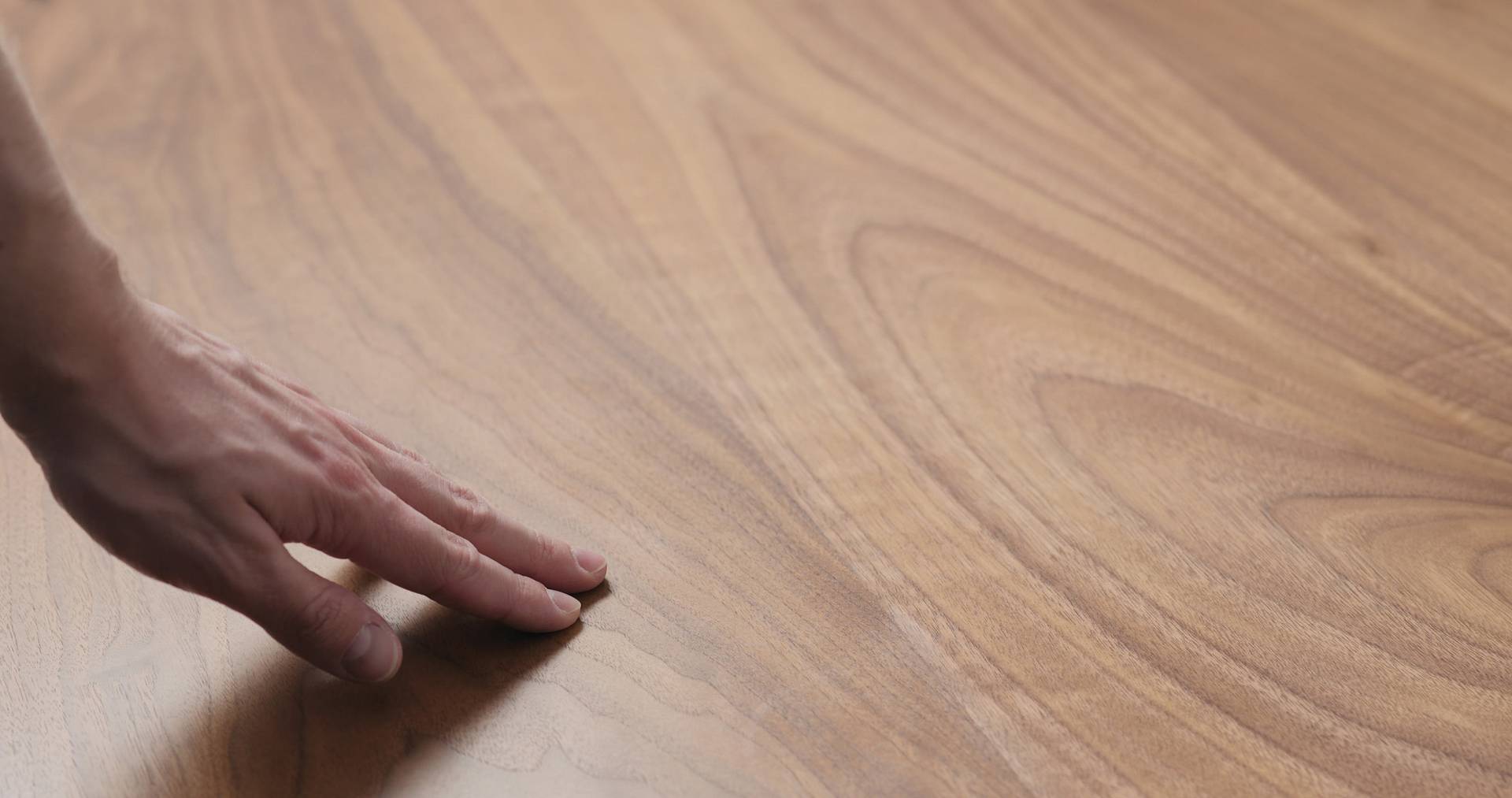 Hand prüft glatte Oberfläche eines geölten Holzbodens mit sichtbarer Maserung