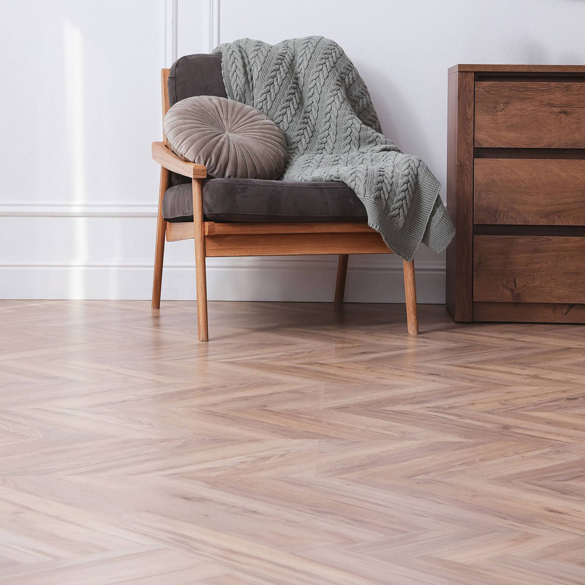 Heller Parkettboden im Fischgrätmuster mit Sessel und Holzkommode