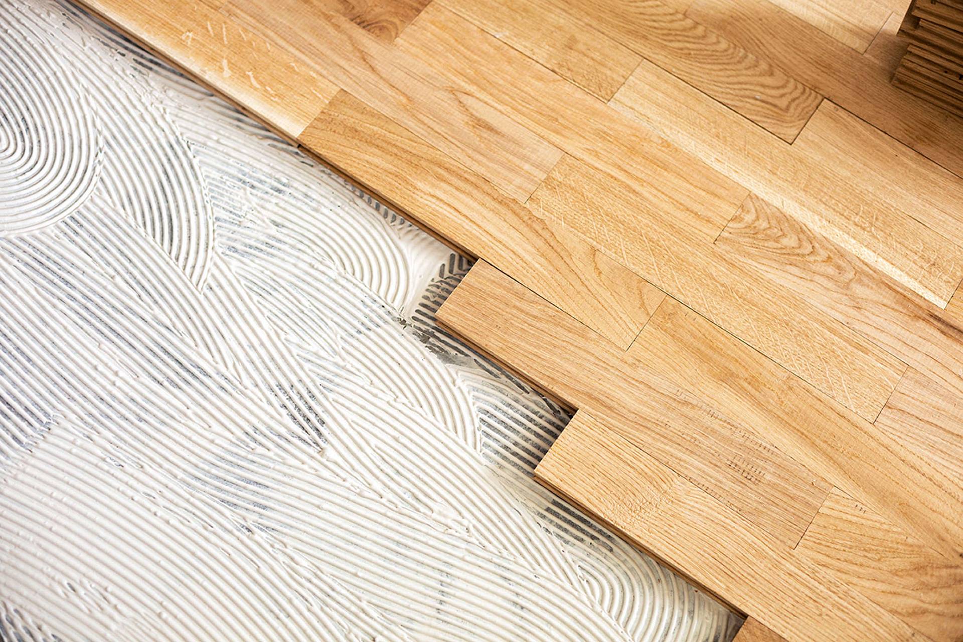 Holzparkett wird in frischen Kleber auf dem Boden verlegt, Zahnspachtel-Struktur ist deutlich sichtbar.