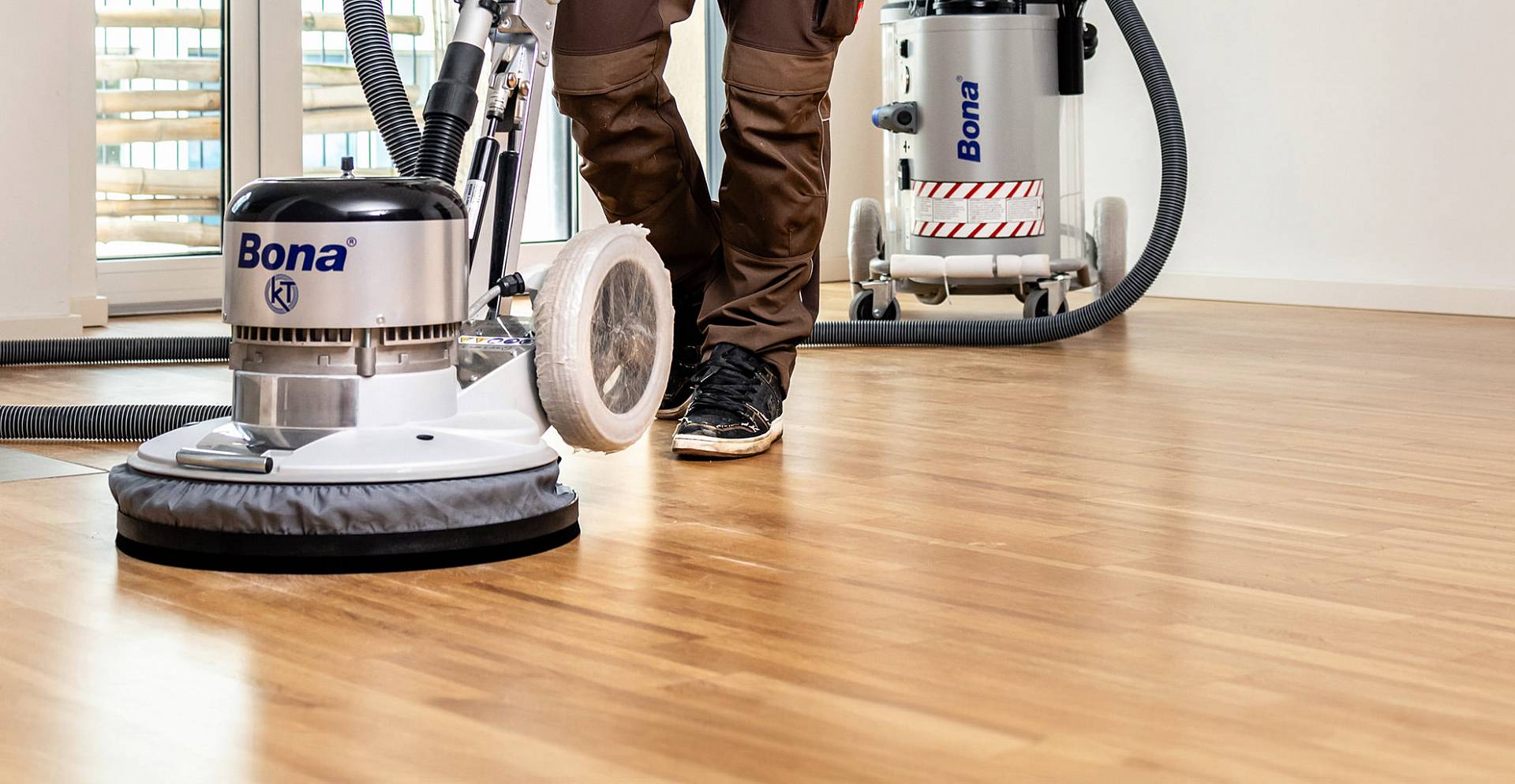 Eine Parkettschleifmaschine wird von einem Handwerker über einen hellen Holzboden geführt, um die Oberfläche gleichmäßig abzuschleifen.