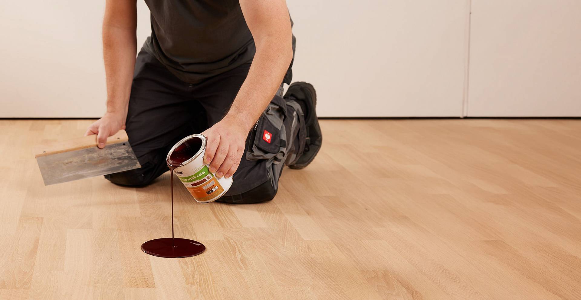 Eine Person kniet auf einem Parkettboden und trägt Holzöl aus einem Behälter gleichmäßig auf die Oberfläche auf.