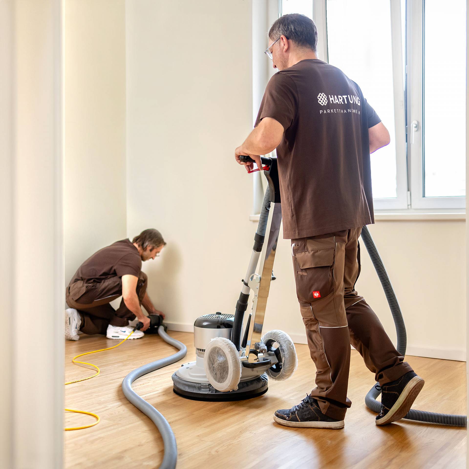 Zwei Handwerker schleifen Parkettboden mit Maschinen im Innenraum