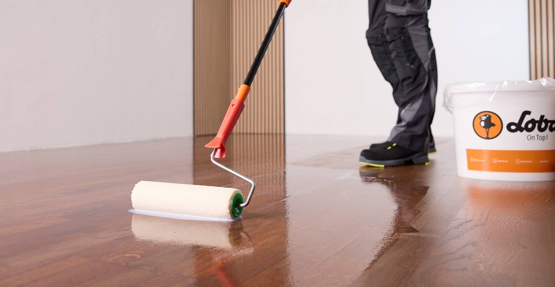 Farbroller trägt glänzenden Lack auf dunklen Parkettboden auf und hinterlässt spiegelnde Oberfläche