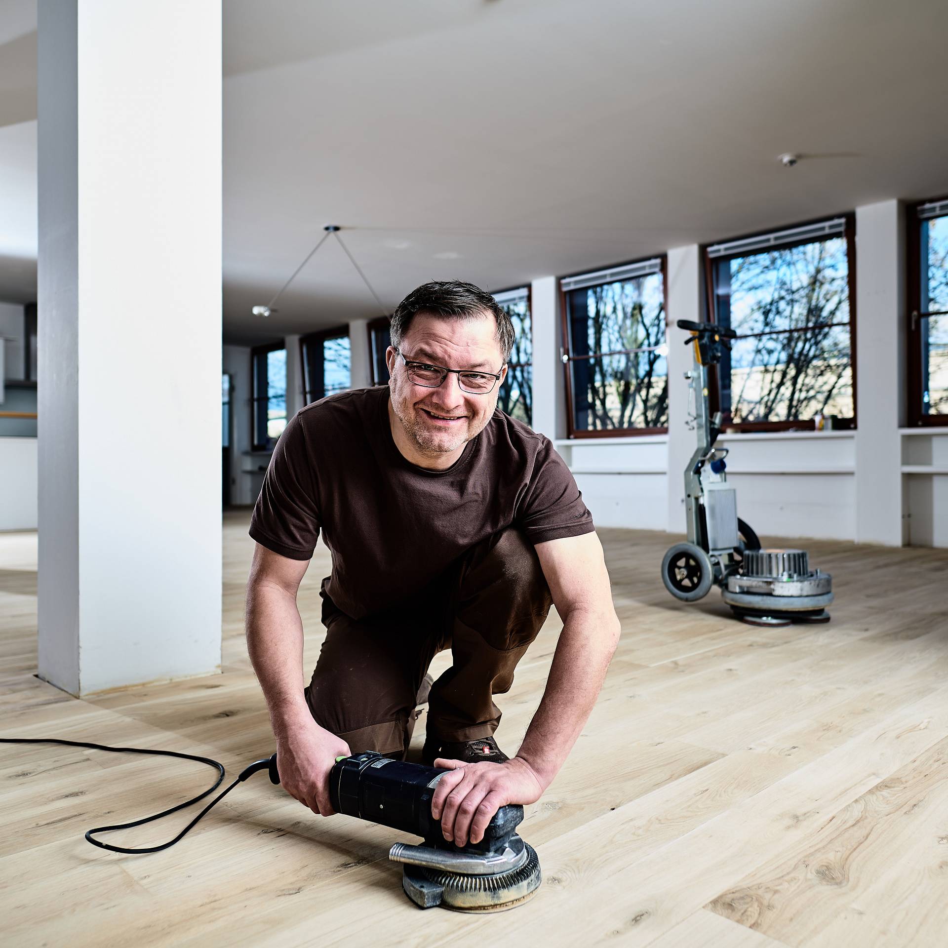 Parkettleger bearbeitet Holzboden mit Randschleifer im hellen Raum