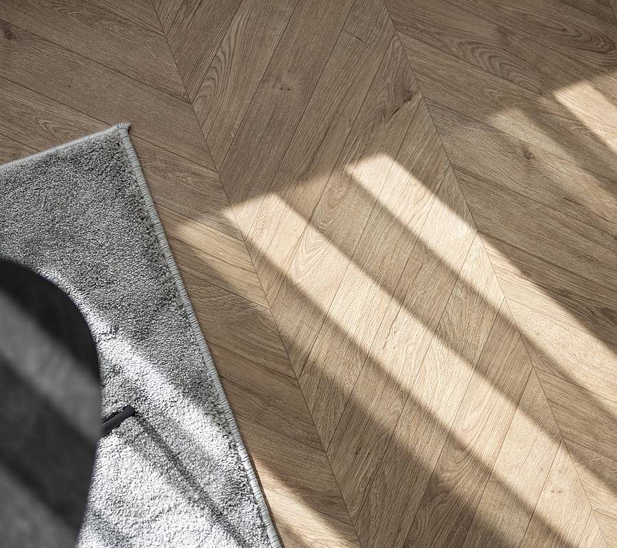 Fischgrätparkett im warmen Tageslicht mit Teppichkante im Vordergrund