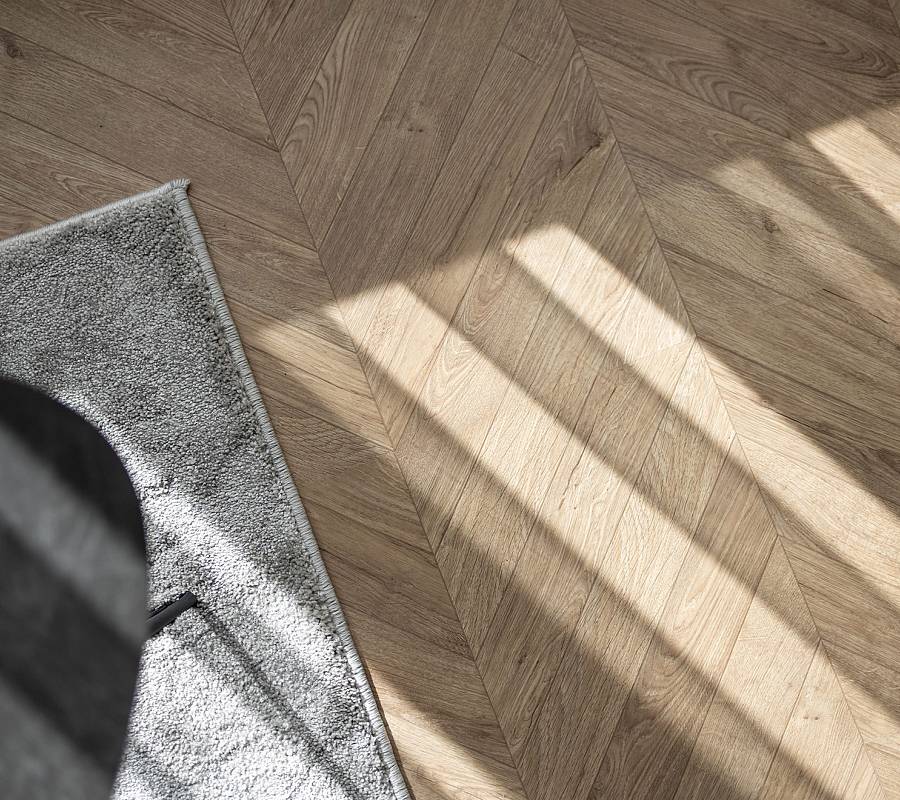 Fischgrätparkett im warmen Tageslicht mit Teppichkante im Vordergrund