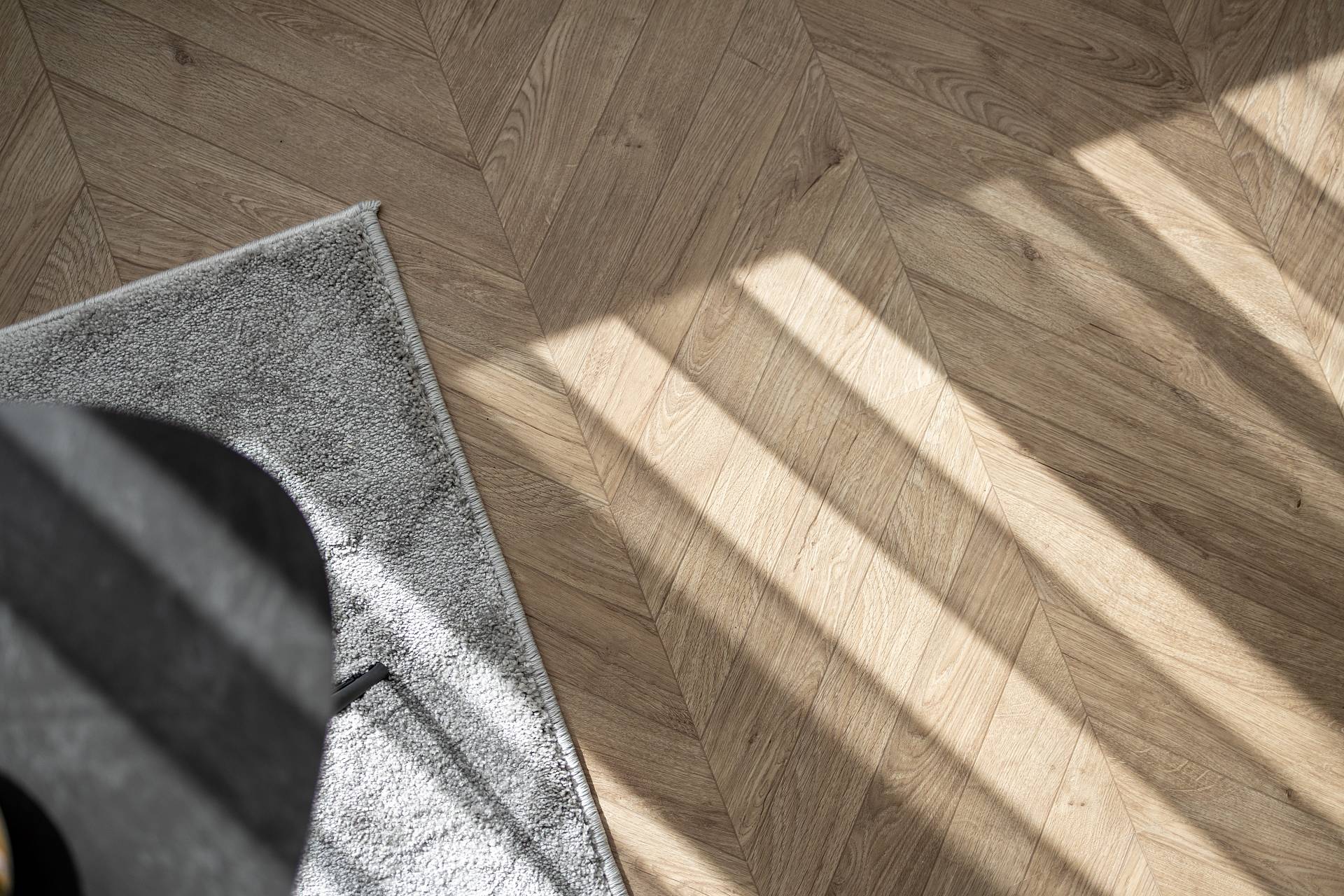 Fischgrätparkett im warmen Tageslicht mit Teppichkante im Vordergrund