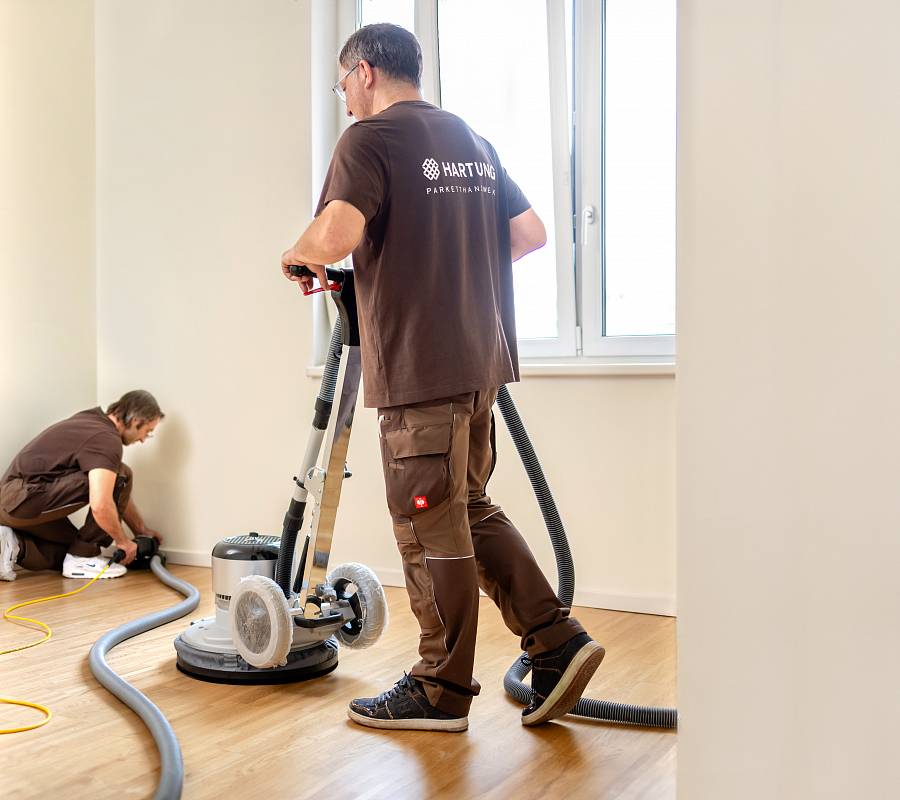 Zwei Parkettleger schleifen Holzboden professionell im hellen Innenraum