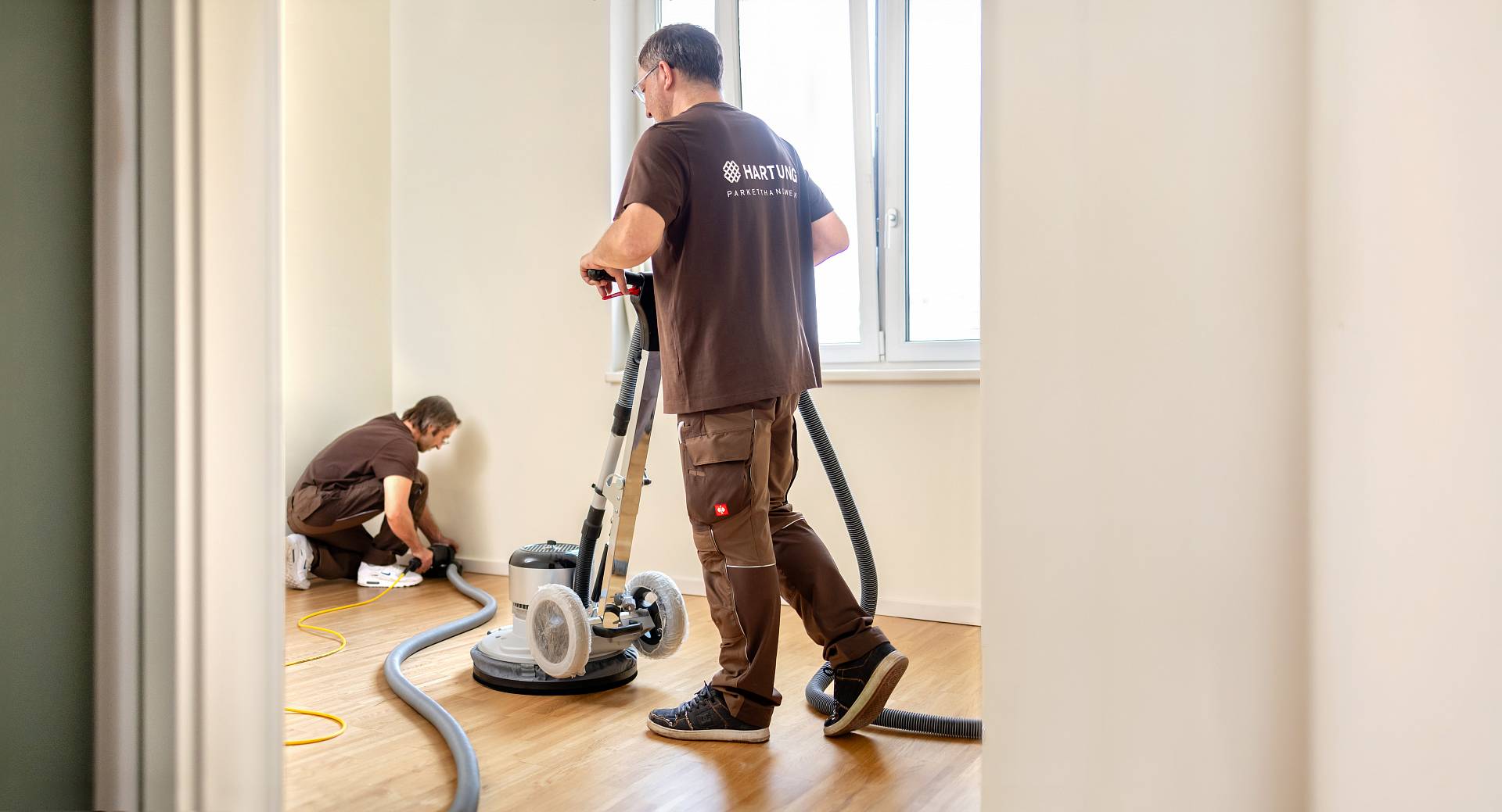 Zwei Parkettleger schleifen Holzboden professionell im hellen Innenraum