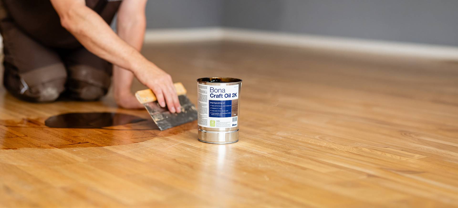 Parkett wird mit Spachtel geölt, Öldose steht im Vordergrund