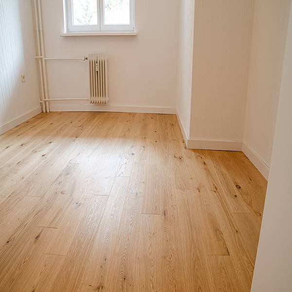 Heller Wohnraum mit breiten Eichen-Landhausdielen, Sofa, Teppich und großen Fenstern mit Blick auf eine städtische Umgebung.
