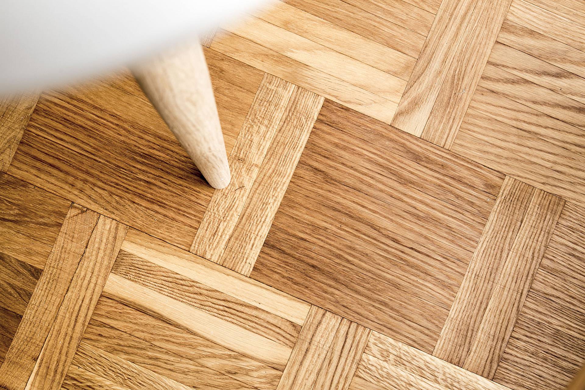 Detailaufnahme eines Parkettbodens mit geometrischem Muster und Möbelbein aus hellem Holz.