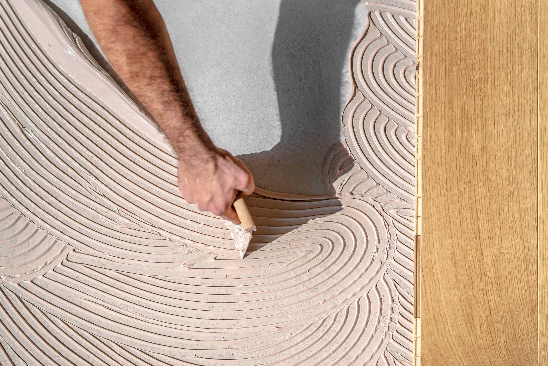 Zahnspachtel verteilt Parkettkleber gleichmäßig auf dem Untergrund