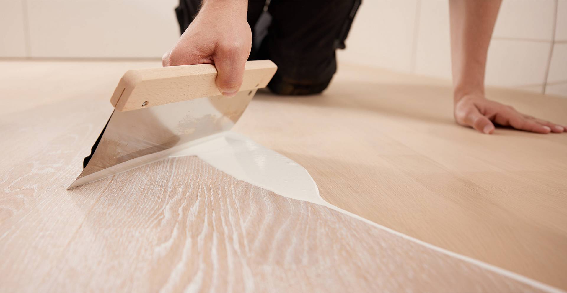 Handwerker trägt mit Spachtel pigmentiertes Öl auf helle Holzdielen auf und verleiht dem Parkett neuen Glanz.