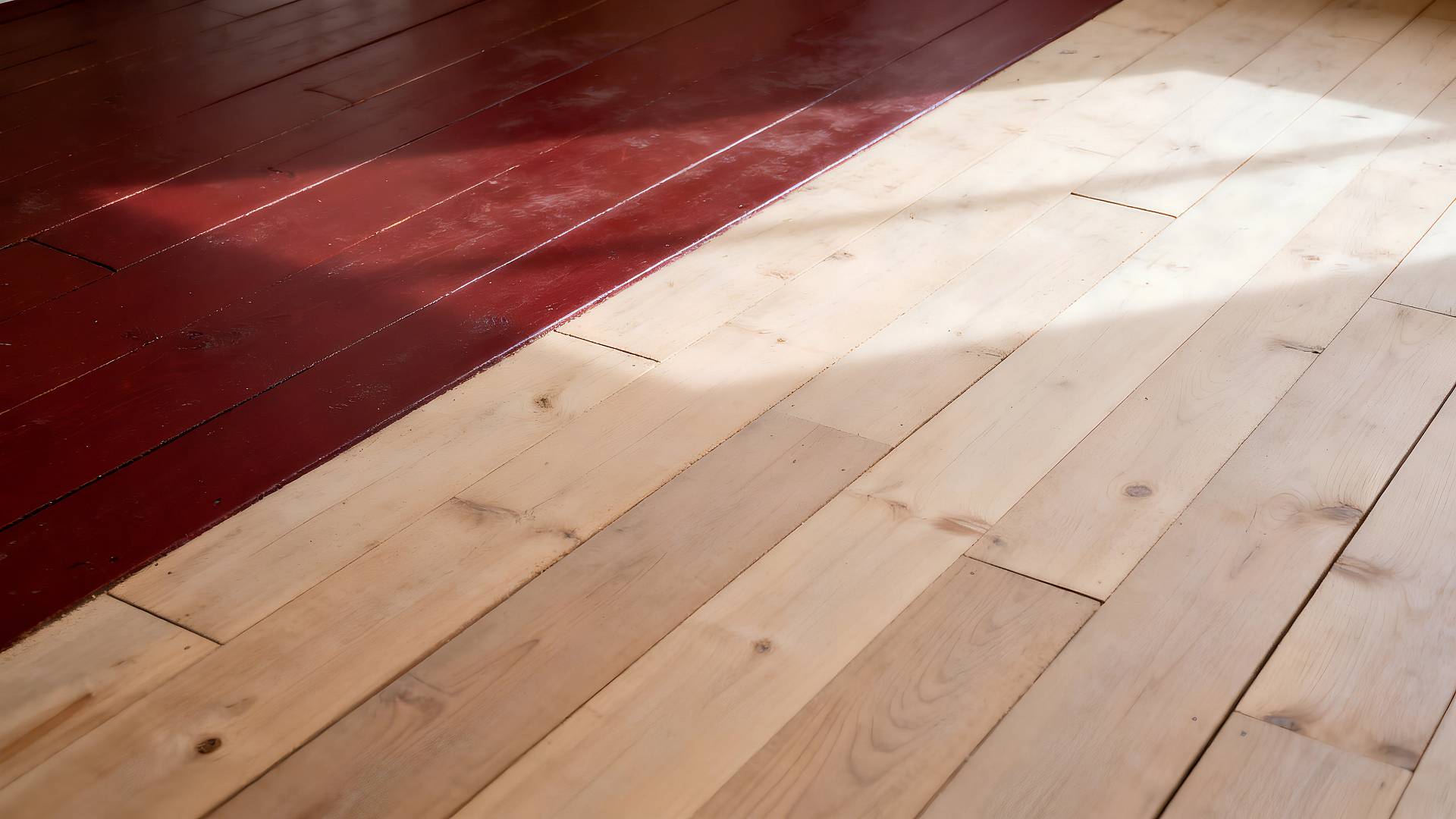 Holzdielenboden mit teils roter Ochsenblut-Beschichtung und teils abgeschliffener, heller Naturholzfläche.