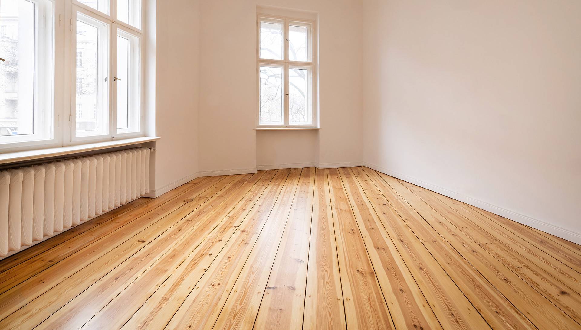 Leerer Raum mit frisch geschliffenen Holzdielen und großen Fenstern