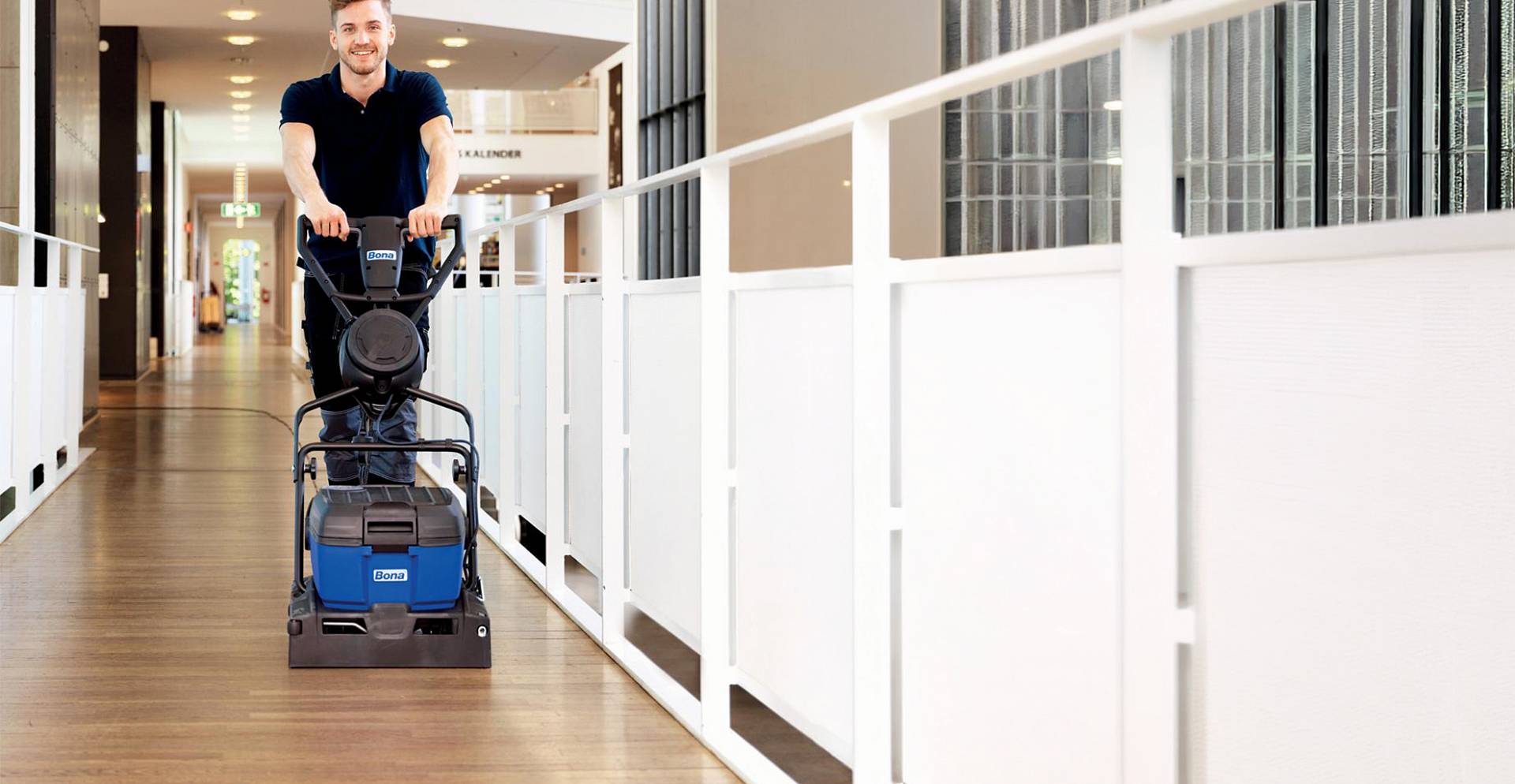 Handwerker reinigt Parkettboden mit professioneller Maschine in modernem Arbeitsgebäude und sorgt für eine gepflegte Oberfläche.