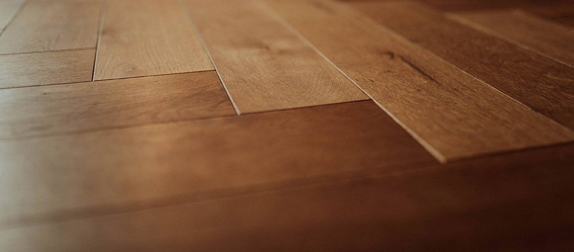 Detailaufnahme eines warm beleuchteten Holzparkettbodens mit diagonal verlegten, glatten Dielen