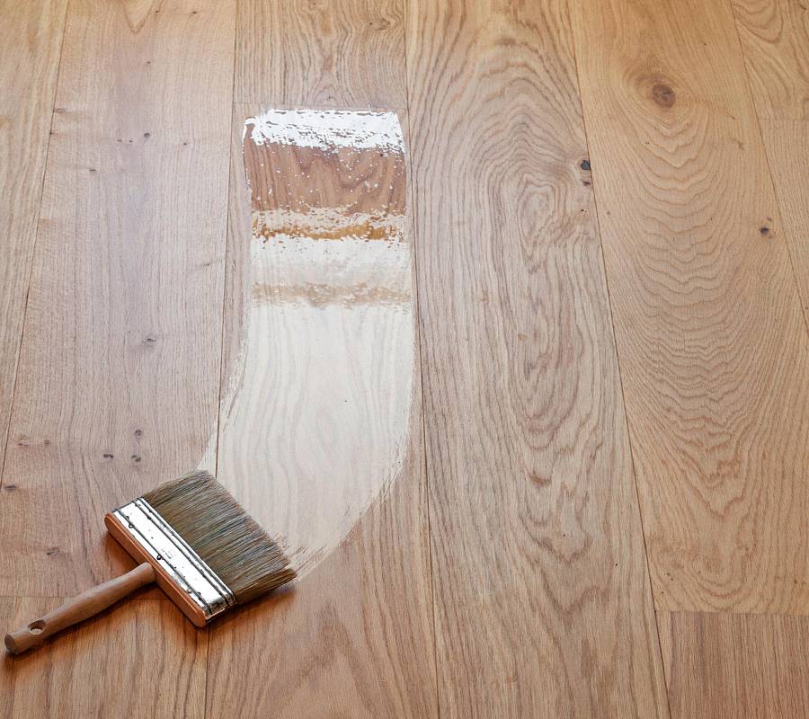 Pinsel trägt Holzöl auf Eichenparkett auf und zeigt Vorher-Nachher-Effekt