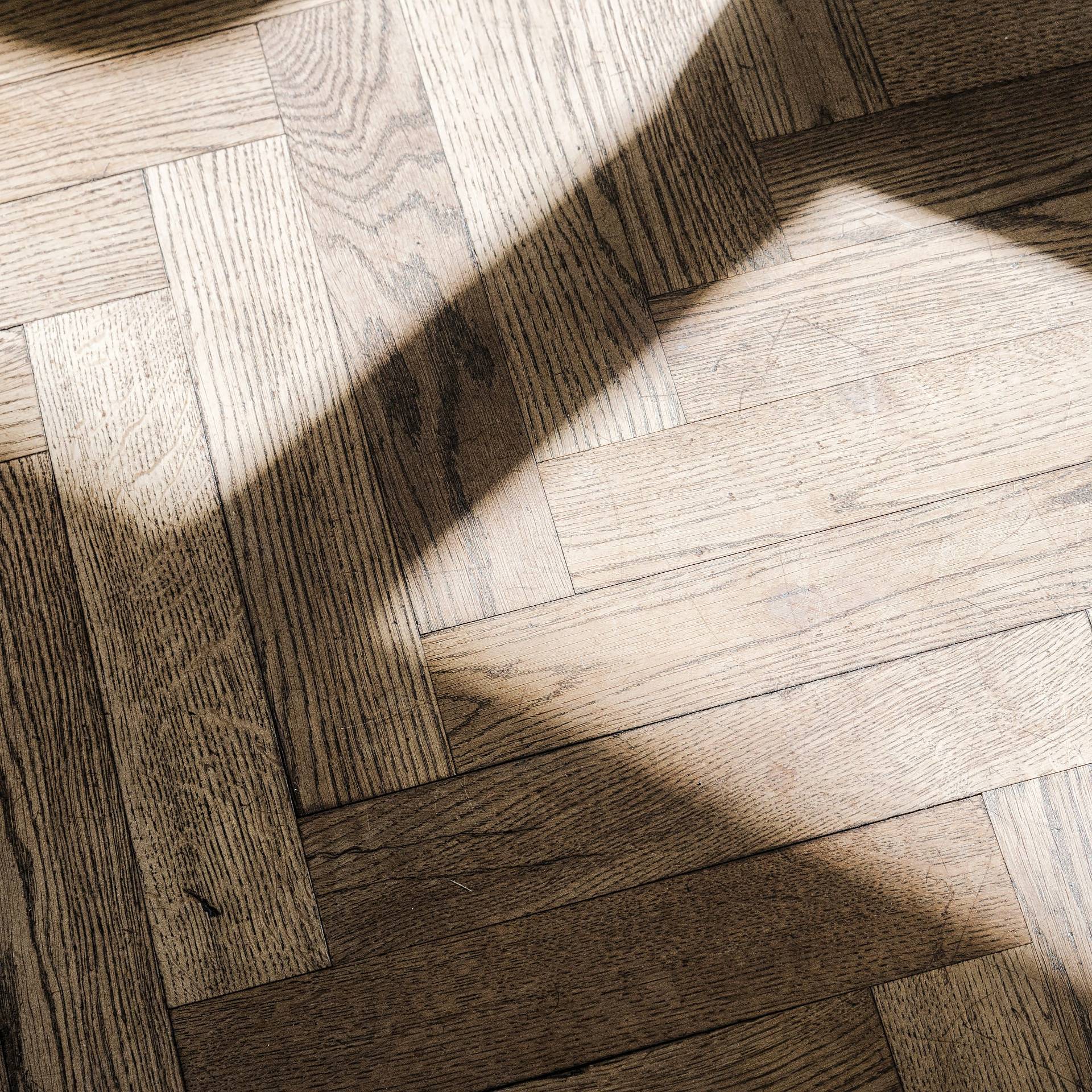 Sonnenlicht fällt auf dunkles Fischgrätparkett mit markanter Maserung