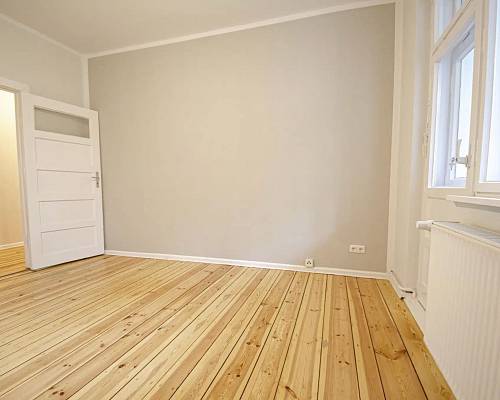 Altbauzimmer mit geschliffenem Dielenboden und weißer Kassettentür