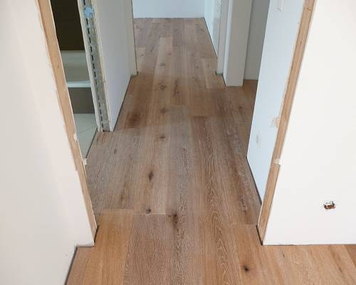 Schmaler Flur mit Eichenparkett und klaren Wandflächen in modernem Neubau.