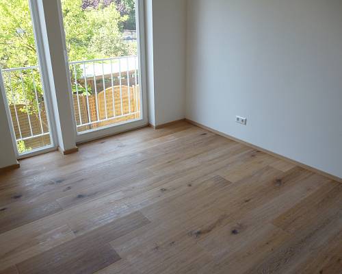 Heller Raum mit breiten Eichendielen und bodentiefen Fenstern.