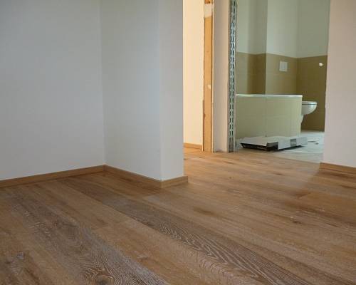 Raum mit Eichen-Landhausdielen und sichtbarer Türöffnung zum Bad.