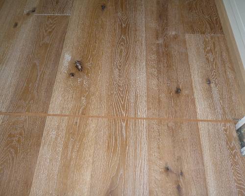 Detailaufnahme eines rustikalen Eichen-Dielenbodens mit markanten Ästen und lebhafter Maserung.