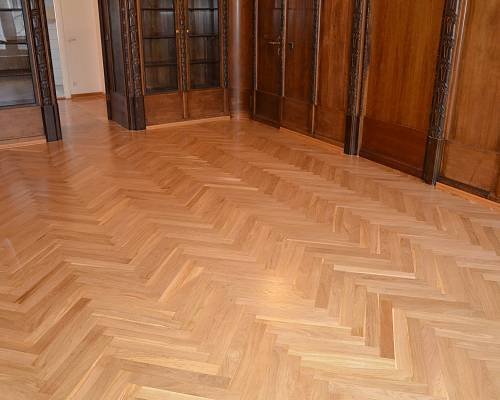 Großzügiger Raum mit aufgearbeitetem Fischgrätparkett und integrierten Vitrinen.