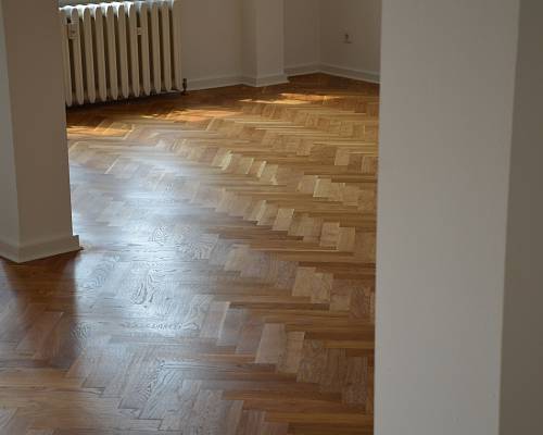 Lichtdurchfluteter Raum mit aufgearbeitetem Parkett und Heizkörper im Hintergrund.