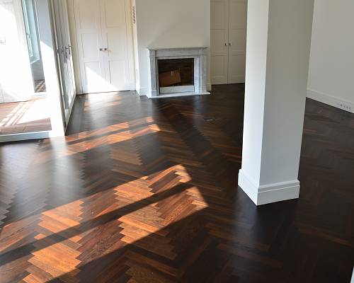 Dunkles Fischgrätparkett mit starkem Lichteinfall und modernem Kamin.