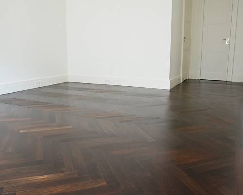 Großzügiger Raum mit dunkel geöltem Fischgrätparkett und weißen Wänden.
