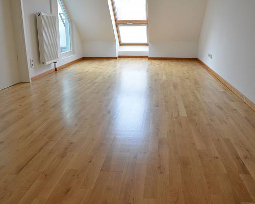 Dachgeschossraum mit großflächigem Parkett und bodentiefem Fenster.