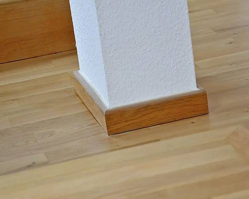 Detail einer Holzsäule mit sauber angearbeitetem Sockel auf Parkett.