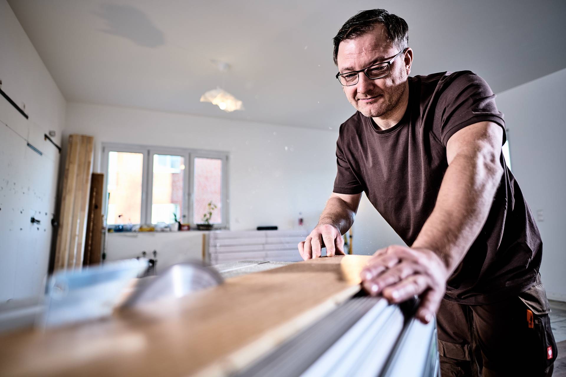 Parkettleger bei der präzisen Bearbeitung von Parkettbrettern in einem hellen Innenraum.